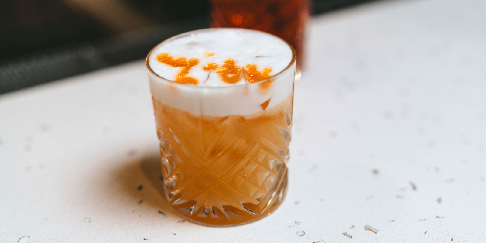 Orange cocktail sitting on a marble countertop.